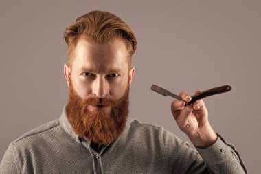 Berber atölyesinde fotokopi odası olan bir adam. Adam tıraş olmak için berber bıçağı tutuyor. Adam gri arka planda berber bıçağıyla tıraş oluyor. Adam berber dükkanında bıçakla tıraş oluyor..