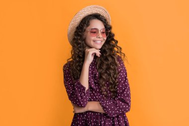 Hasır şapkalı ve güneş gözlüklü neşeli çocuk. Sarı arka planda uzun esmer kıvırcık saçlı..