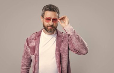 Erkek giyim kuşamında karizmatik beyaz adam. Gri arka planda izole edilmiş erkek kıyafetleri içinde şık bir adam. Stüdyoda erkek giyim bölümünde şık bir adam. Erkek giyim kuşamında şık bir adamın fotoğrafı..