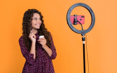 Uzun kıvırcık saçlı mutlu çocuk blogcu blog holding pudra fırçası videosu yapıyor.