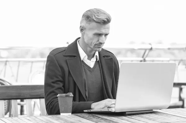 Serious director man in formalwear working online in laptop in outdoor cafe.
