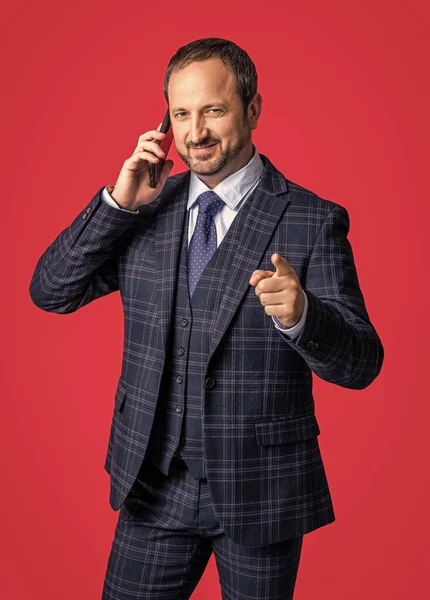 businessman in talk on smartphone pointing finger. photo of businessman in talk on smartphone. businessman in talk on smartphone isolated on red background. businessman in talk on smartphone in studio