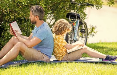 Baba oğul açık havada kitap okuyarak kaynaşıyor. Baba oğul okuma zamanı. Baba ve çocuk birlikte kitap okuyor. Oğlu babasıyla dışarıda öğreniyor. Açık havada hikaye zamanı..