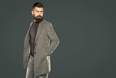 Sakallı, olgun bir adam gri arka planda rahat giyinir..