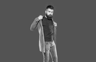 Yakışıklı, sakallı, olgun bir adam gri arka planda rahat giyinir..