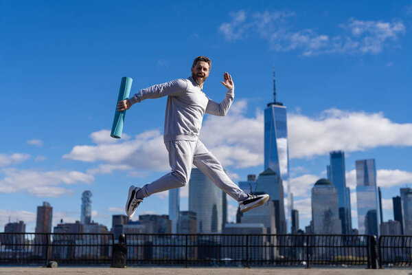 Sportsman athlete man jumping with energy in New York with fitness mat for morning workout outdoor.