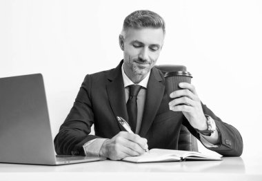 Olgun bir ofis çalışanı iş ofisinde yazı yazıyor ve kahve içiyor..