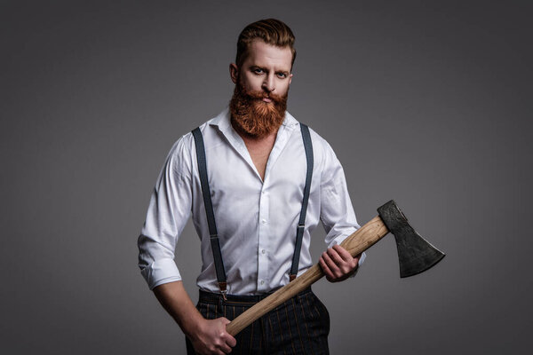 Brutal male fashion style. Male brutality. Vintage brutality guy with axe in retro suspenders. Brutal man in suspenders isolated on grey. Mature redhead man with hairstyle. Physical Brutality.