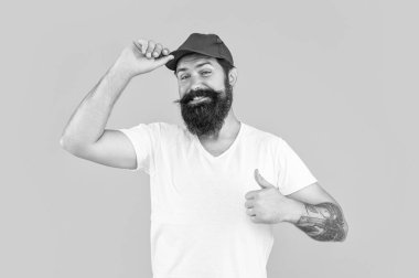 Sarıda izole edilmiş sakallı teslimatçı, başparmağını kaldır. Stüdyodaki sakallı teslimatçı. Arka plandaki sakallı teslimatçı. Sakallı teslimatçının şapkalı fotoğrafı..