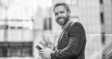 Açık havada akıllı telefondan mesaj atan mutlu bir adam. Adam sokakta akıllı telefondan mesaj atıyor. Dışarıda akıllı telefondan mesaj atan bir adam var. Akıllı telefondan ceketle mesajlaşan adamın fotoğrafı..