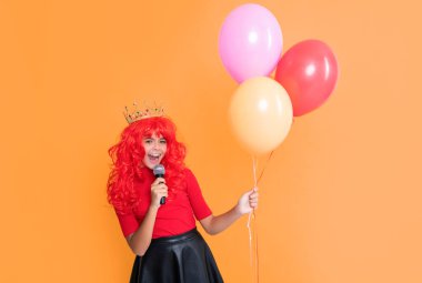positive child in crown with microphone and party balloon on yellow background.