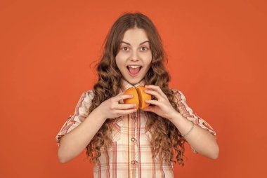 surprised teen girl hold citric fruit on orange background.