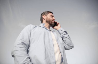 Telefonda erkek erkeğe konuşma. Adam akıllı telefondan konuşuyor. Gökyüzü arka planında insan iletişimi.