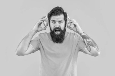 Şaşırmış adamın sarı kulaklıklı yüksek sesli müziği var. Sinirli adam kulaklıkla yüksek sesle müzik dinler. Yüksek sesli kulaklıklı rahatsız bir adam. Yüksek sesli müzikle rahatsız bir adamın stüdyo çekimi..