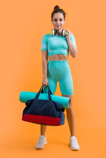 positive fitness woman in sportswear with sport bag in studio. fitness woman in sportswear isolated on yellow background. fitness and sportswear.