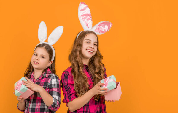 smiling easter children in bunny ears hold present box on yellow background with copy space.