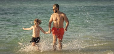 Baba oğul bağ kurma ilişkisi. Baba oğul deniz sahilinde koşuyor. Baba oğul, yaz tatilinin tadını çıkarıyor. Birlikte iyi eğlenceler. Baba ve oğul arasında denizde özel anlar.