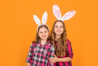 Sarı arka planda tavşan kulaklı neşeli Paskalya çocukları.