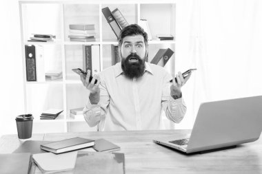 İki elinde de cep telefonu olan şaşırmış bir adam ofis masasında oturuyor, seçim senin..