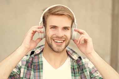 man smile listening music outdoor. man listening music outside. man listening music and wearing checkered shirt. photo of man listening music in headphones.