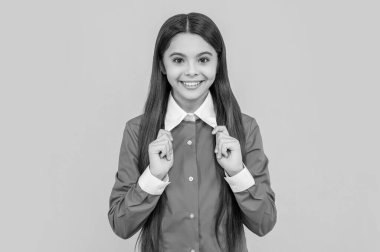 Sarıda izole edilmiş mutlu liseli kız. Stüdyodaki genç kız. Arkaplanda genç bir kız var. Üniformalı bir genç kızın fotoğrafı..