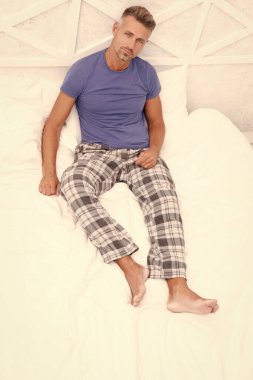 Man enjoying rest in bed. Man resting in bed. Man having rest in morning. Man in pajamas relaxing on white bedclothes. Morning rest.