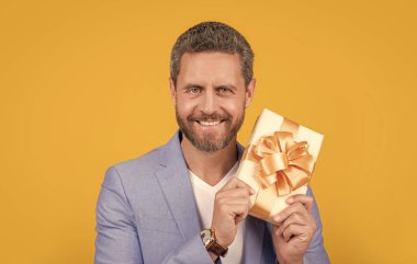 happy guy with gift box for holiday. photo of guy holding occasion gift box. guy hold gift box isolated on yellow background. guy hold gift box in studio.