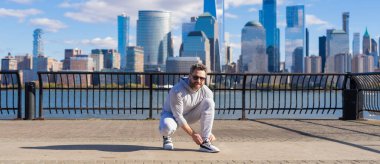 Sporcu antrenmana hazırlanıyor. Ayakkabılarını giyip yerde oturuyor. Spor ayakkabılarını bağlayan sporcu. Atletik ayakkabılar. Spor ayakkabısı kravat bağcıkları dışarıda. Spor ayakkabılarının bağcıklarını bağlayan spor adamı. Yarışa hazır..