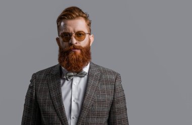 Smokinli, sakallı, şık erkek giyimli, takım elbiseli ve papyonlu bir adam. Gri, fotokopi alanında izole edilmiş..