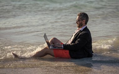 Dizüstü bilgisayarı olan bir iş adamı yaz tatilinde deniz haftasonu tatilinde ve uzaktan bağımsız bir işte çalışıyor..