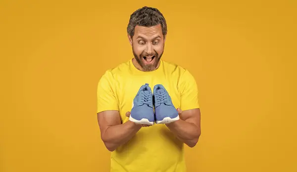 stock image shocked fitness man with sneakers isolated on yellow. fitness man with sneakers on background. fitness man with sneakers in studio. photo of fitness man with sneakers shoes.