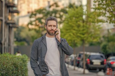 man call on mobile stands outside. photo of man call on mobile phone. man has mobile call outdoor. man having mobile call in the street.