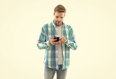 caucasian man texting on phone isolated on white background. casual man texting on phone in studio. man texting on phone wearing checkered shirt. photo of man texting on phone device.