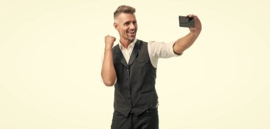 Takım elbiseli mutlu yönetici kazanan jest yapıyor. Cep telefonundan görüntülü arama yapıyor..