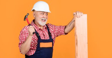 happy aged man woodworker in helmet on yellow background.