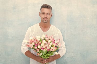 mature man with spring tulips isolated on blue background. photo of man with spring tulips. man with spring tulips. man with spring tulips in studio.