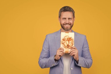 positive guy hold gift box in studio. guy with gift box for holiday. photo of guy holding occasion gift box. guy hold gift box isolated on yellow background.