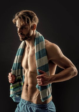 Kaslı bir adam, gri arka planda izole edilmiş karın kasları var. Stüdyoda kaslı bir adam var. Kaslı adam karın kaslarına havlu takıyor. Adamın kaslı karın kaslarının fotoğrafı..