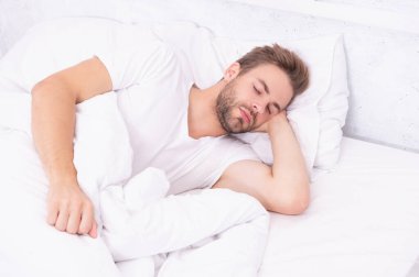 Uykulu adam beyaz yatak odasında uyuyor. Uyuyan genç adam uyuyor. Rahat bir yatakta huzur içinde dinleniyor. Kapalı gözlerle yalan söylemek. Derin erkek uykusu. Geceleri uyuyan bir adam. Huzurlu bir uyku..