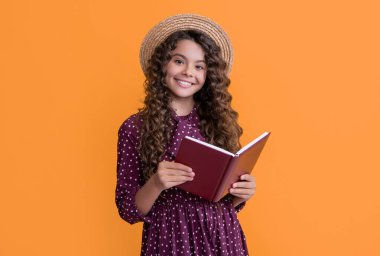 Kıvırcık saçlı çocuk gülüşü sarı arka planda kitap okuyor.