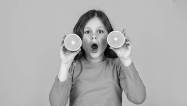 Sarı arka planda portakal meyvesi tutan hayrete düşmüş genç kız..