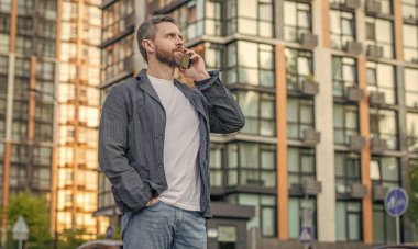 image of man call on mobile phone. man has mobile call outdoor. man having mobile call in the street. man call on mobile outside.