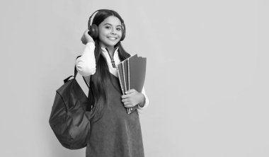 Okul çantalı, kulaklıklı mutlu çocuk. Çalışma kitabı sarı arka planda..