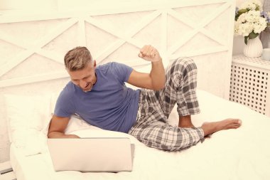 Memnuniyetle evde dizüstü bilgisayarlı serbest çalışan bir adamın fotoğrafı. Evde serbest çalışan bir adam var. Adam evde, yatakta serbest çalışıyor. Adam evde, yatak odasında serbest çalışıyor..