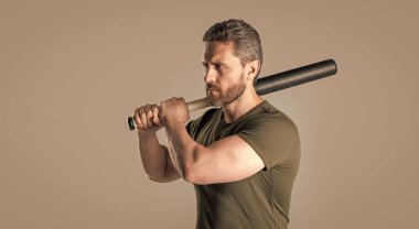 Kızgın adamın saldırganlığı stüdyoda sopayla dövüldü. Sopayı tutan kızgın adamın fotoğrafı. Kızgın adam tehdit ediyor. Öfkeli adam öfkesini gri arka planda yalnız yarasayla ifade eder.