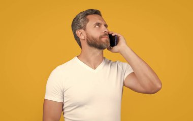 Düşünen adam iletişim akıllı telefonunda konuşur. Adam akıllı telefon konuşmaları yapıyor. İletişim konsepti. Akıllı telefondan konuşan adam sarıda izole edilmiş. Stüdyoda adam akıllı telefonda konuşur..