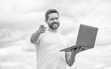 olumlu adam gökyüzü arka planında dizüstü bilgisayarda çalışıyor.