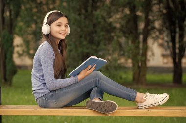 concept of teen. Happy teen girl reading and listening to audiobook in headphones after school outdoors, teen.