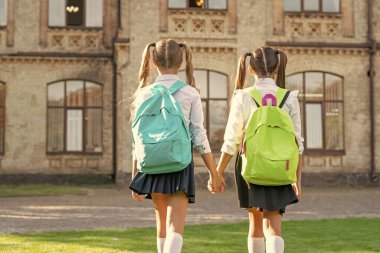 back view of two children with school backpack walking together outdoor. copy space.