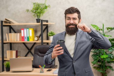 Gülümseyen sakallı iş adamı ofiste fotokopi yeri ve sabah kahvesi ile paket kahve içiyor..